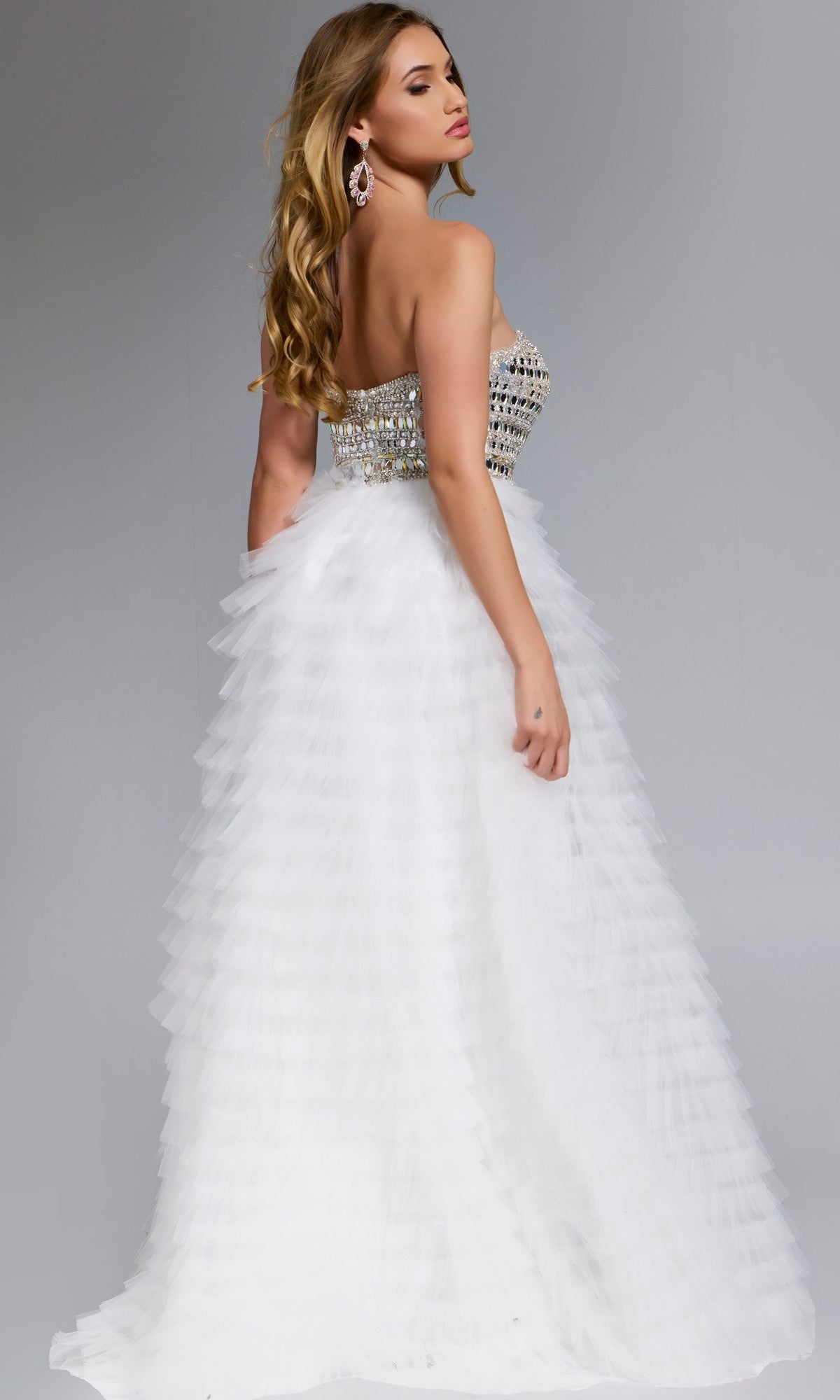 A woman in the Jovani 43412 long prom dress with a strapless beaded corset bodice and ruffle tulle skirt stands against a plain gray background, facing slightly away.
